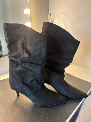 Svarta slouchy stövletter med klack - Säljer ett par helt oanvända svarta stövletter med slouchy skaft och spetsig tå från lefties i Spanien. Skorna har smal klack på ca 6,5 cm och är i mockaliknande material. 