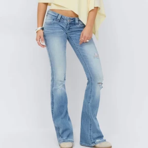 Low waist tall Gina jeans - Snygga ljusblå bootcut jeans med slitna detaljer och lätt utsvängda ben. Jeansen har klassisk femficksdesign och låg midja. Perfekta för en avslappnad och trendig look.
