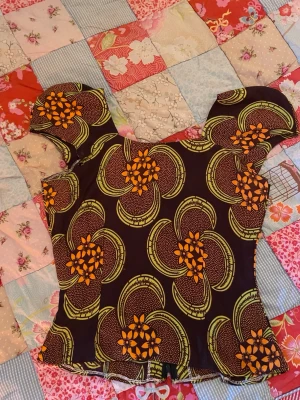 Blommig topp med puffärmar - Färgstark topp med blommigt mönster i orange och grönt på mörk botten, 70tals stil. Figurnära passform med dragkedja i ryggen. 