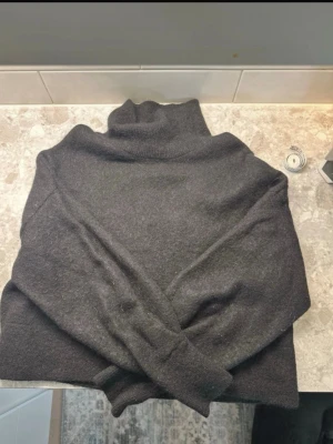 Svart polotröja i ull material - Mysig svart ull polotröja med lång ärm och hög krage. Perfekt för lager-på-lager och enkel att matcha med olika outfits. Tröjan har en klassisk rak passform. 