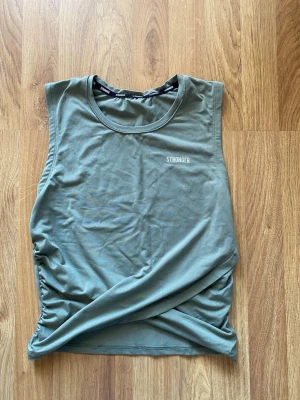 Grön ärmlös linnetopp från Stronger - Snygg grön linnetopp från Stronger med rund halsringning och diskret logga på bröstet. Toppen är ärmlös och har en enkel, sportig design som passar perfekt till träning eller chill dagar. Tillverkad i mjukt och stretchigt material för maximal komfort. Lappen avklippt men skulle säga att den passar som S.