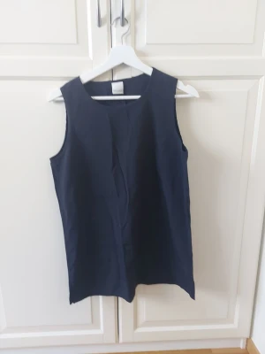 Mörkblå ärmlös linnetopp från SHARE - Stilren mörkblå linnetopp från SHARE med enkel, rak passform och rund halsringning. Toppen är ärmlös och har en minimalistisk look som passar perfekt till både jeans och kjol. Materialet känns lätt och svalt, perfekt för varma dagar.