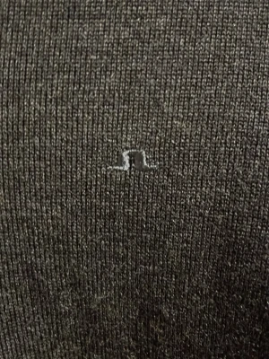 Mörkgrå tröja från J.Lindeberg - Snygg mörkgrå tröja från J.Lindeberg med diskret logga broderad på bröstet. Tröjan har V-ringning och är tillverkad i ett mjukt, tunt stickat material som känns skönt mot huden. Perfekt för lager-på-lager och stilrena outfits. Nypris 1500kr.