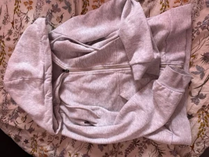 Ljusgrå zip hoodie - Ljusgrå hoodie med dragkedja framtill och stor huva. Tillverkad i mjukt sweatshirtmaterial med ribbade muddar vid ärmslut och nederkant. Perfekt för en avslappnad och chill stil.