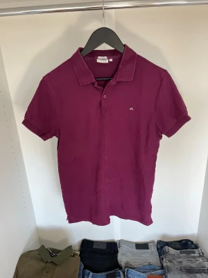 Vinröd pikétröja från J.Lindeberg - Säljer en vinröd pikétröja från J.Lindeberg i slim fit-modell. Tröjan har klassisk krage, korta ärmar och liten broderad logga på bröstet. Tillverkad i bomull för en skön känsla och snygg passform. Hör gärna av dig vid frågor!