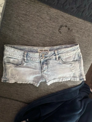 Ljusblå jeansshorts från Tally Weijl - Säljer ett par ljusblå jeansshorts från Tally Weijl med slitna detaljer och råa kanter. Shortsen har fem fickor, bälteshällor och dubbla knappar framtill. Perfekta för varma dagar och en avslappnad stil.