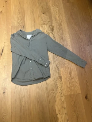Grön linneskjorta - Stilren grön skjorta med volangkrage och knappar framtill. Skjortan har långa ärmar med manschett och är tillverkad i ett mjukt material som känns bekvämt mot huden. Perfekt för en trendig och avslappnad look. Passar perfekt till sommaren