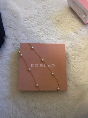 Guldfärgat halsband med pärlor EDBLAD - Snyggt halsband från EDBLAD med tunn guldfärgad kedja och flera vita pärlor jämnt fördelade längs kedjan. Perfekt accessoar för att lyfta din outfit med en elegant touch.