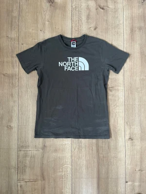 Svart t-shirt från The North Face - Snygg svart t-shirt från The North Face med stor vit logga på bröstet och mindre logga på ryggen. Klassisk rund hals och korta ärmar. Tillverkad i mjuk bomull som känns skön mot huden. Perfekt för en avslappnad och stilren look.