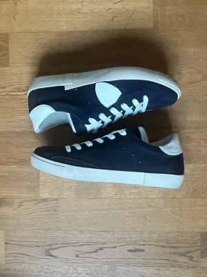 Philippe Model svarta sneakers - Snygga sneakers från Philippe Model i svart mocka med vita detaljer och vit sula. Klassisk låg modell med vita skosnören och logotyp på sidan. Perfekta för dig som gillar stilrena och trendiga skor.