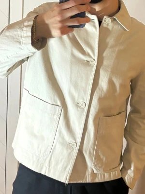 Zara Beige overshirt - Stilren beige overshirt med klassisk krage och fyra knappar framtill. Två stora utanpåfickor ger en avslappnad look. Tillverkad i ett kraftigare bomullstyg som passar perfekt till lager-på-lager. Enkel och clean design utan synligt märke.