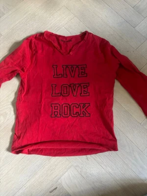 Röd långärmad t-shirt Zadig & Voltaire - Cool röd långärmad t-shirt från Zadig & Voltaire med trycket 'LIVE LOVE ROCK' på framsidan. T-shirten har en lätt v-ringad hals med knappdetalj och är gjord i mjuk bomull. Perfekt för dig som gillar rockig stil.