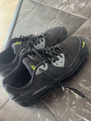 Nike Air Max svart/grå sneakers - Säljer ett par Nike Air Max sneakers i svart och grått med neon-gula detaljer. Skorna har lågt skaft, mesh och mocka-material samt klassiska Air Max-sulan. Snygga prickiga skosnören och tydlig Nike-logga på tungan och hälen.