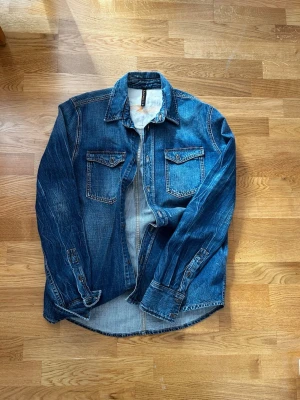 Nudie Jeans Jeanjacka - Säljer en riktigt snygg jeansjacka/jeansskjorta, den har ett par lagningar två vid armbågarna och en under kragen. Personligen tycker jag att det gör den ännu snyggare! Hör av er vid funderingar, vid snabb och smidig affär diskuterar vi priset!