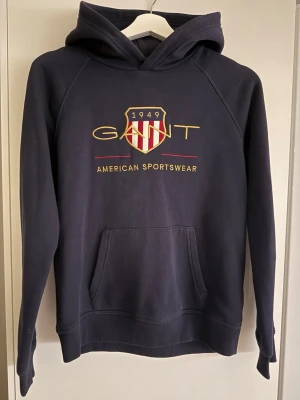 Mörkblå hoodie från GANT - Säljer en super snygg äkta Gant hoodie då den aldrig blivit använd och inte kommer till användning.   •Skick: helt ny , inga skavanker alls  •Storlek:158/164 passar en XS! •Färg: Mörkblå   Snabb frakt!  Pris kan diskuteras!