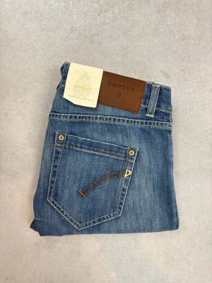Blå slim fit jeans från Dondup - Snygga blå jeans från Dondup i slim fit-modell med klassisk femficksdesign och läderpatch bak i midjan. Jeansen har ljus tvätt och kontrastsömmar, perfekta till en avslappnad stil. Tillverkade i bomull med en skön stretch.