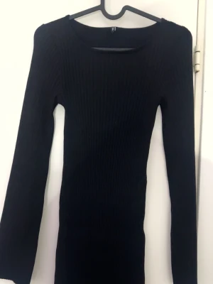 Svart ribbad långärmad klänning - En svart, ribbad klänning med lång ärm och rund halsringning. Klänningen är figurnära och har en enkel, stilren design som passar perfekt till många olika tillfällen, klänning anpassar sig jättebra med din kroppsform