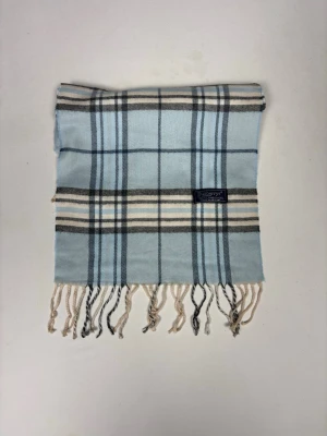 Ljusblå rutig halsduk från Burberry - Supersnygg halsduk från Burberry i ljusblått med klassiskt rutmönster i svart, vitt och beige. Tillverkad i mjuk lammull och har fransar i ändarna. Perfekt accessoar för att lyfta din outfit med en touch av lyx.