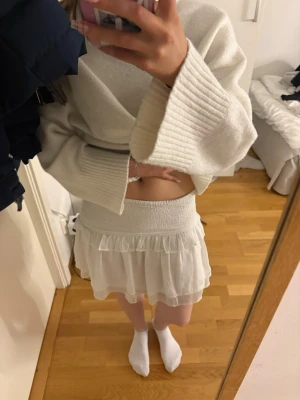 Vit volangkjol - Supersöt vit kortkjol med volangdetaljer och bred resår i midjan. Kjolen har en luftig och flowy känsla, perfekt för varmare dagar. Passar till både stickade tröjor och crop tops för en fräsch look. priset kan diskuteras❤️❤️