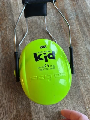 3M Peltor Kid hörselkåpor neon - Säljer ett par neonfärgade hörselkåpor från 3M Peltor Kid. De har en starkt grön färg, justerbar metallbåge och svart vaddering för extra komfort. Perfekta för att skydda öronen mot höga ljud på konserter eller andra evenemang.