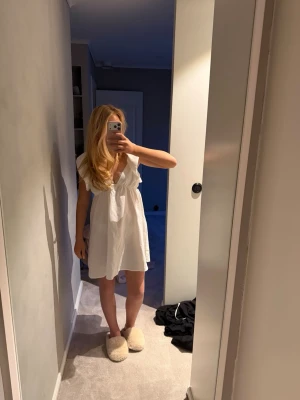 Vit studentklänning med volang och knyt - Söt vit kortklänning med volangdetaljer på axlarna och v-ringad fram. Klänningen har öppen rygg med knytband och är ärmlös. Perfekt för studenten eller skolavslutningen. Oanvänd men utan prislapp!!💖💖