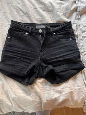 Svarta denimshorts från Amisu - Svarta jeansshorts från Amisu med klassisk femficksdesign och uppvikta benslut. Shortsen har hög midja och stängs med knapp och dragkedja. Perfekta för en avslappnad och trendig look.