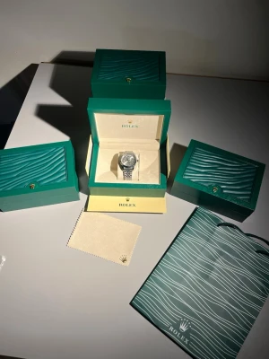 Herr klock - Fullsett  - Modell: Datejust Skick: Ny, Oanvänd  Utförande: Oysterlänk i stål, räfflad bezel, ljus urtavla Tillbehör: Komplett set – originalbox, certifikat, manualer, tags och påse