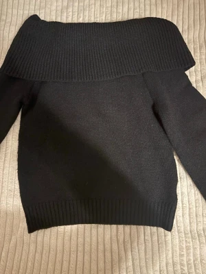 Svart off shoulder stickad tröja - Snygg svart stickad tröja med bred off shoulder-krage och långa ärmar. Tröjan har ribbstickade muddar vid ärmslut och nederkant, vilket ger en stilren och modern look. Perfekt för dig som vill ha en trendig och bekväm stickad topp. Ärmarna lite utsvängda och nästan aldrig använd. 