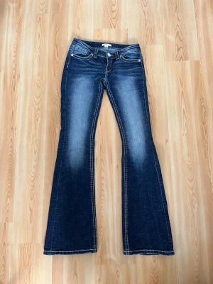 Blå bootcut jeans från Gina Tricot - Snygga blå bootcut jeans från Gina Tricot med klassisk femficksdesign och markerade sömmar. Jeansen har en lätt tvättad look och utsvängda ben, perfekta för en trendig och avslappnad stil.