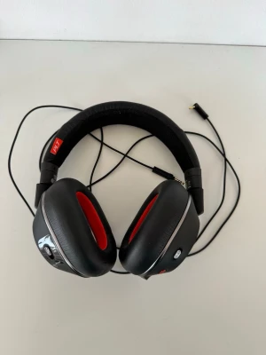 Plantronics svarta over-ear hörlurar - Snygga over-ear hörlurar från Plantronics i svart med röda detaljer. Mjuka öronkuddar och vadderat huvudband i tyg för extra komfort. Sladdanslutning med 3,5 mm kontakt. Perfekta för musik, gaming eller videosamtal. Även full noice cancelling 