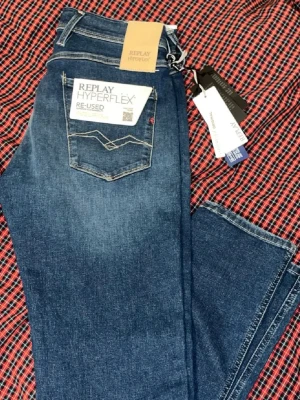 Blå Replay Hyperflex jeans - Snygga blå jeans från Replay Hyperflex-serien med klassisk femficksdesign och raka ben. Jeansen har en cool tvättad look och är tillverkade i stretchigt material för extra komfort. Perfekta för dig som vill ha både stil och rörelsefrihet. Storleken är w27 l32 men dom sitter mer som w28-w29 med tanke på att det är hyperflex 
