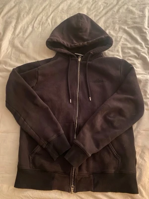 Svart zip-hoodie från J.Lindeberg - Svart hoodie med dragkedja från J.Lindeberg. Klassisk modell med tryck på framsidan. Bra skick, inga skador osv. Stl S men sitter lite större. Hör av er om ni har några frågor.