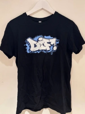 DIF tröja  - Svart t-shirt med coolt graffiti-inspirerat tryck i vitt och blått på bröstet där det står 'Diff!'. Klassisk passform och rund halsringning, perfekt för en streetwear-look.