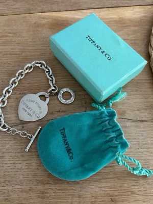 Tiffany & Co. Armband i Sterling Silver - Elegant Return to Tiffany™ Heart Tag armband i sterling silver (925). Klassisk modell från 1960-talet med hjärtberlock och robust kedja som ger en tidlös och exklusiv känsla.  Armbandet är i fint skick med normal, vintage användning och vacker silverglans. Gravyren är tydlig med stämpeln ”T & Co 925”. Låset fungerar perfekt och känns stabilt, precis som det ska på Tiffany-smycken.  Perfekt present till dig själv eller någon du håller kär. Original dustbag och kartong medföljer ej.   Nypris 8000k