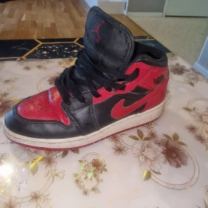 Nike Air Jordan 1 Bred svart/röd 38 - Säljer ett par ikoniska Nike Air Jordan 1 i färgen svart och röd, även kallad 'Bred'. Skorna har klassisk snörning, rund tå och är tillverkade i skinn med tydliga Air Jordan-detaljer på sidan. Perfekta för dig som gillar streetwear och sneakers med attityd. 