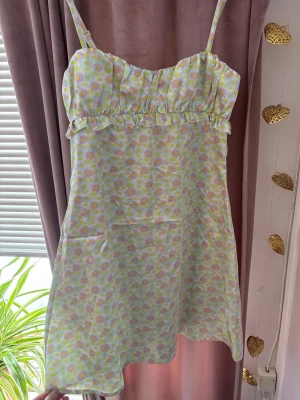 Blommig sommarklänning Blanche Olia - Söt blommig klänning från Blanche Olia med tunna axelband och volangdetalj under bysten. Superfin korsett ryggdetalj. Klänningen har ett pastelligt mönster i ljusgrönt, gult och lila på glansigt tyg. Perfekt för varma dagar och ger en fräsch och ungdomlig vibe. Kostar 2876kr nypris💗Storlek S