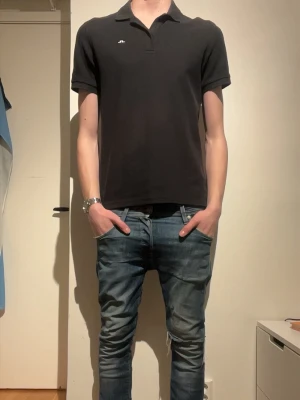 Svart pikétröja från J.Lindeberg - Klassisk svart pikétröja från J.Lindeberg med krage och korta ärmar. Tröjan har en liten logga på bröstet och är tillverkad i ett mjukt bomullsmaterial. Perfekt för en stilren och avslappnad look. Modellen på bilden är 185. Priset är inte hugget i sten🙌🔥💸