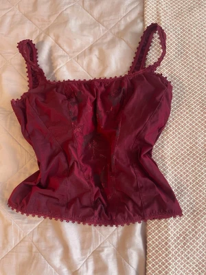 Vinröd topp med spetsdetaljer - Toppen är lätt croppad och har insydd bysthållare. Den är i bra skick och har inga defekter.