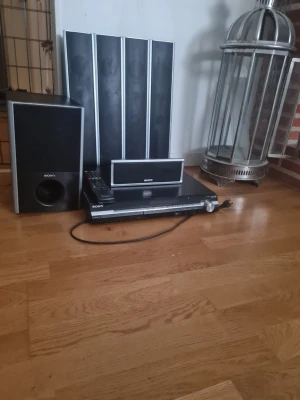 Sony hemmabiosystem med högtalare - Säljer ett komplett Sony hemmabiosystem med flera högtalare, subwoofer, centerhögtalare och fjärrkontroll. Systemet är svart med silverdetaljer och har en stilren, rektangulär design. Perfekt för dig som vill ha grymt ljud till film och musik.
