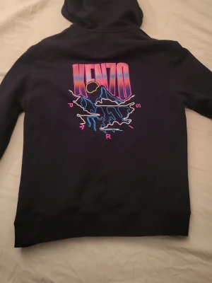 Svart Kenzo sip hoodie Limited Edition  - Svart hoodie från Kenzo med dragkedja och huva. På ryggen finns ett stort färgglatt neontryck med Kenzo-logga och grafiskt motiv i rosa, blått och gult. Framtill finns en mindre logga i samma stil. Perfekt för dig som gillar streetwear och snygga detaljer.