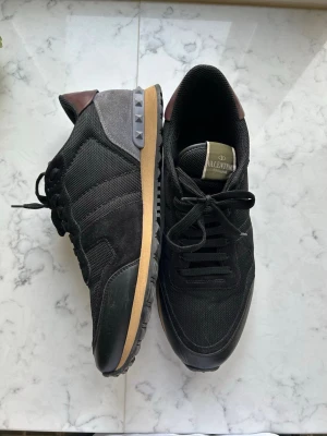 Svarta Valentino sneakers med nitar - Valentino Garavan Rockrunner Storlek: 44 Färg: Svart, grå & burgundy Ett par perfekta grisch skor inför våren & sommaren! Skick: 9/10, några väldigt småa märken på det svarta gummi, annars är de perfekta! Ny pris: 600€ Skickar inom 24h!