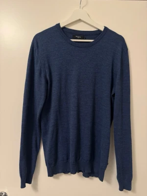 Blå stickad tröja från Matinique - Mörkblå stickad tröja från Matinique med rund halsringning och långa ärmar. Tröjan har en enkel och stilren design med ribbade muddar vid ärmslut och nederkant. Perfekt för lager på lager och passar till det mesta. Storlek: L
