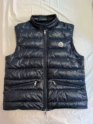 Moncler Gui Väst - Säljer denna riktigt fräscha Gui västen. Den har använts någon enstaka gång men är i suveränt skick. Den är storlek 3 men passar en M/L. Givetvis så är den äkta vilket bekräftas i sista bilden✅ Skriv vid fler frågor och funderingar🙌