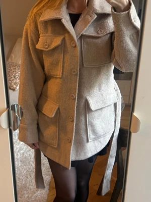 Kort knytbar jacka  - Kort knytbar beige jacka med skärp från NA-KD. Använd fåtal gånger. 