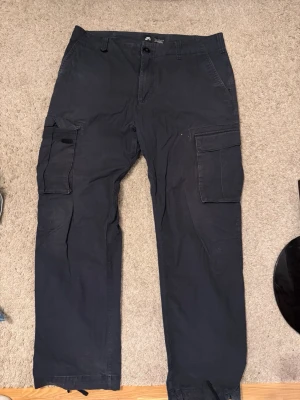 Svarta cargobyxor med fickor - Snygga svarta cargobyxor med klassiska stora benfickor på båda sidor. Byxorna har rak passform och stängs med knapp och dragkedja. Perfekta för en avslappnad och trendig stil.