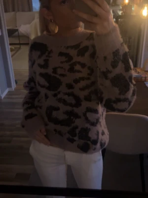 Beige leopardmönstrad stickad tröja - Säljer en beige stickad tröja med svart leopardmönster. Tröjan har rund halsringning, långa ärmar och en avslappnad passform. Perfekt för dig som gillar djurmönstrat och vill ha något både snyggt och bekvämt.
