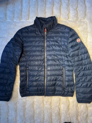 Mörkblå Colmar jacka  - Snygg och stilren Colmar Originals quiltad jacka i mörkblå färg. Perfekt som vår-/höstjacka eller som lätt vinterjacka. Tidlös design som funkar både till vardag och mer uppklätt. ✔️ Storlek: 48 (motsvarar:S, M)✔️ Passform: Normal✔️ Färg: Mörkblå✔️ Skick: Bra begagnat skick✔️ Detaljer: – Två fickor med dragkedja – Hel dragkedja framtill – Lätt vadderad och bekväm – Diskret Colmar-patch på ärmen ℹ️ Notera: Loggan är något sliten (se bild), men jackan är äkthetsverifierad av Certiaglo. 📦Fraktas snabbt.