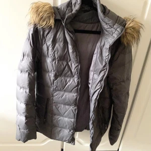 Grå Vinterjacka  - Säljer min vinterjacka i storlek 34. Jackan har en huva med pälskrage som är (fejk). Bra skick på jackan och mörkgrå till färgen. 