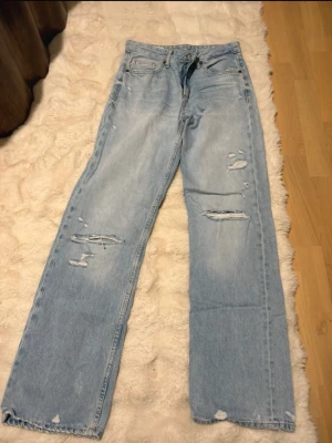 Ljusblåa raka slitna jeans från Zara - Säljer ett par ljusblå jeans med raka ben och flera slitningar framtill och baktill. Jeansen har klassisk femficksmodell och är tillverkade i denim. Perfekta för en avslappnad och trendig look.