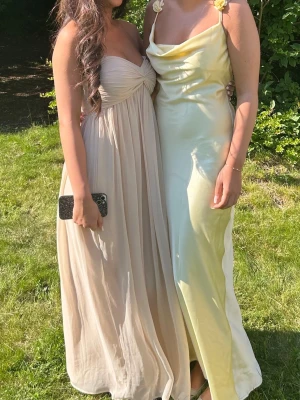 balklänning  - Elegant långklänning i champagnefärg med omlottdetalj över bysten. Klänningen har ett luftigt, svepande fall och markerad byst. Perfekt för sommarens speciella tillfällen. 1,60 på bilden utan klackar💗